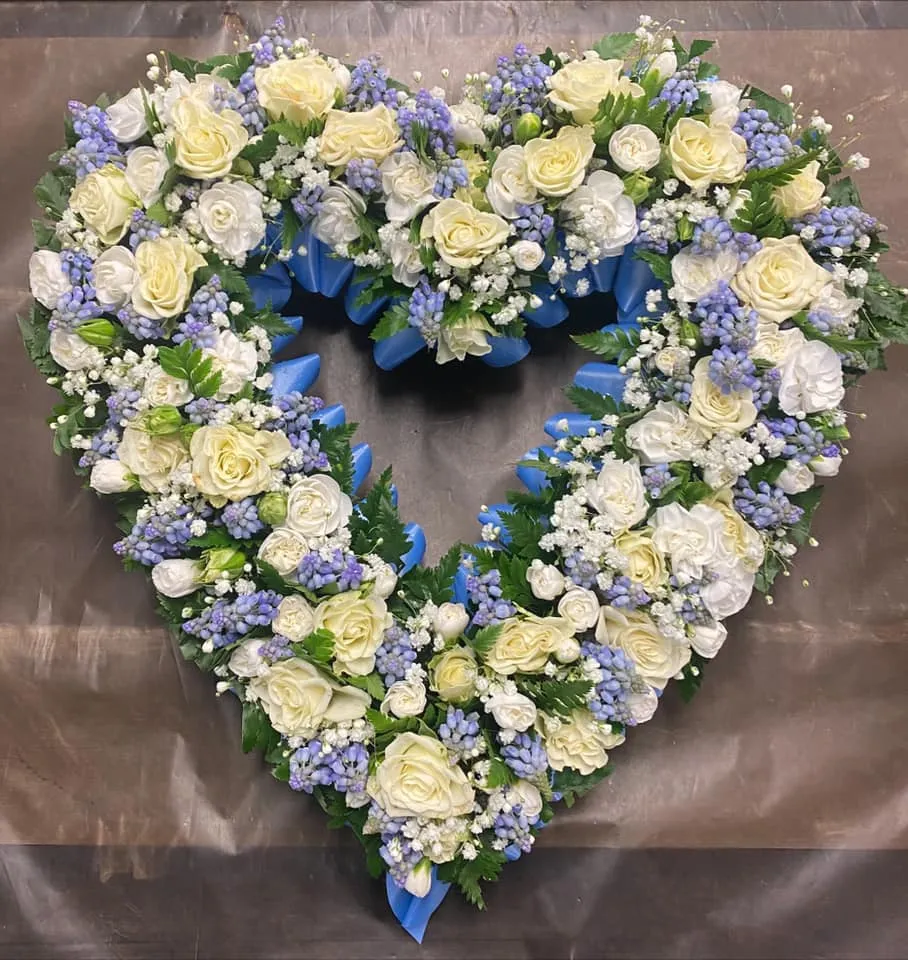 A heart shaped arrangement of white and blue flowers.