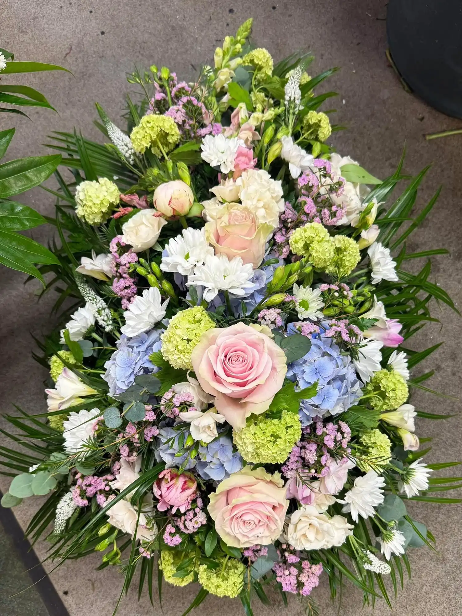 Bouquet of mixed flowers including pink roses, white daisies, blue hydrangeas, and green foliage on a floor.