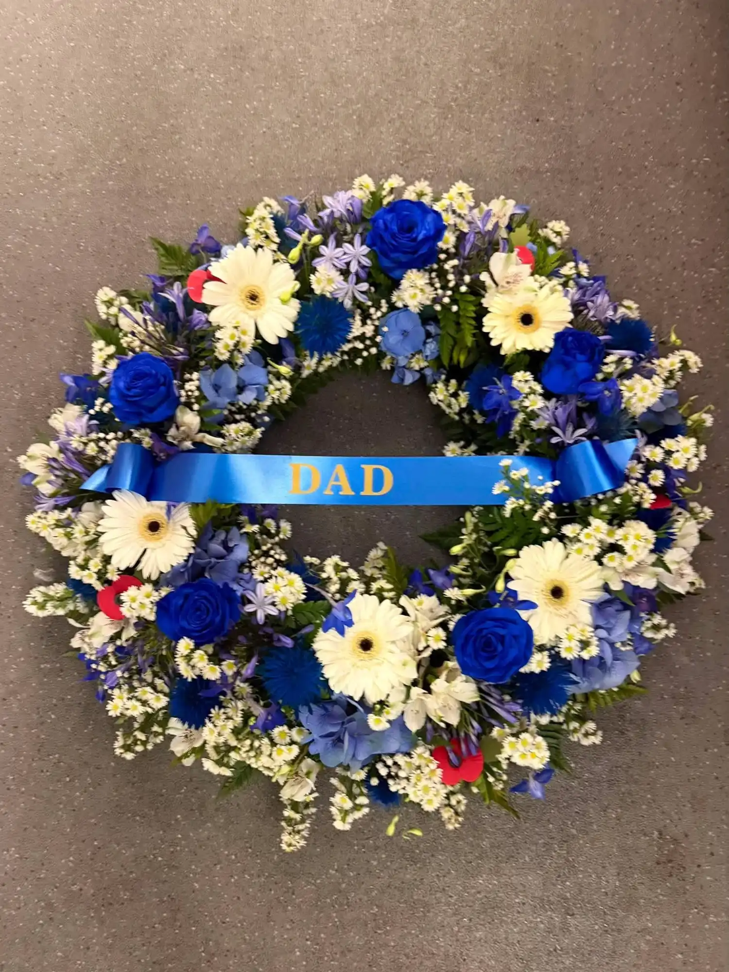 Floral wreath with white and blue flowers and a blue ribbon that says DAD.