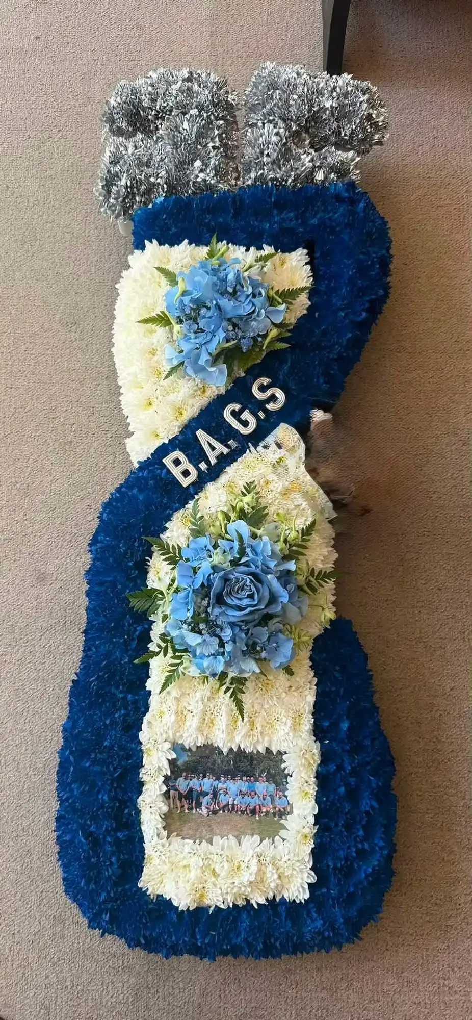 Large golf bag-shaped floral tribute with BAGS letters, blue and white flowers, and a team photo.