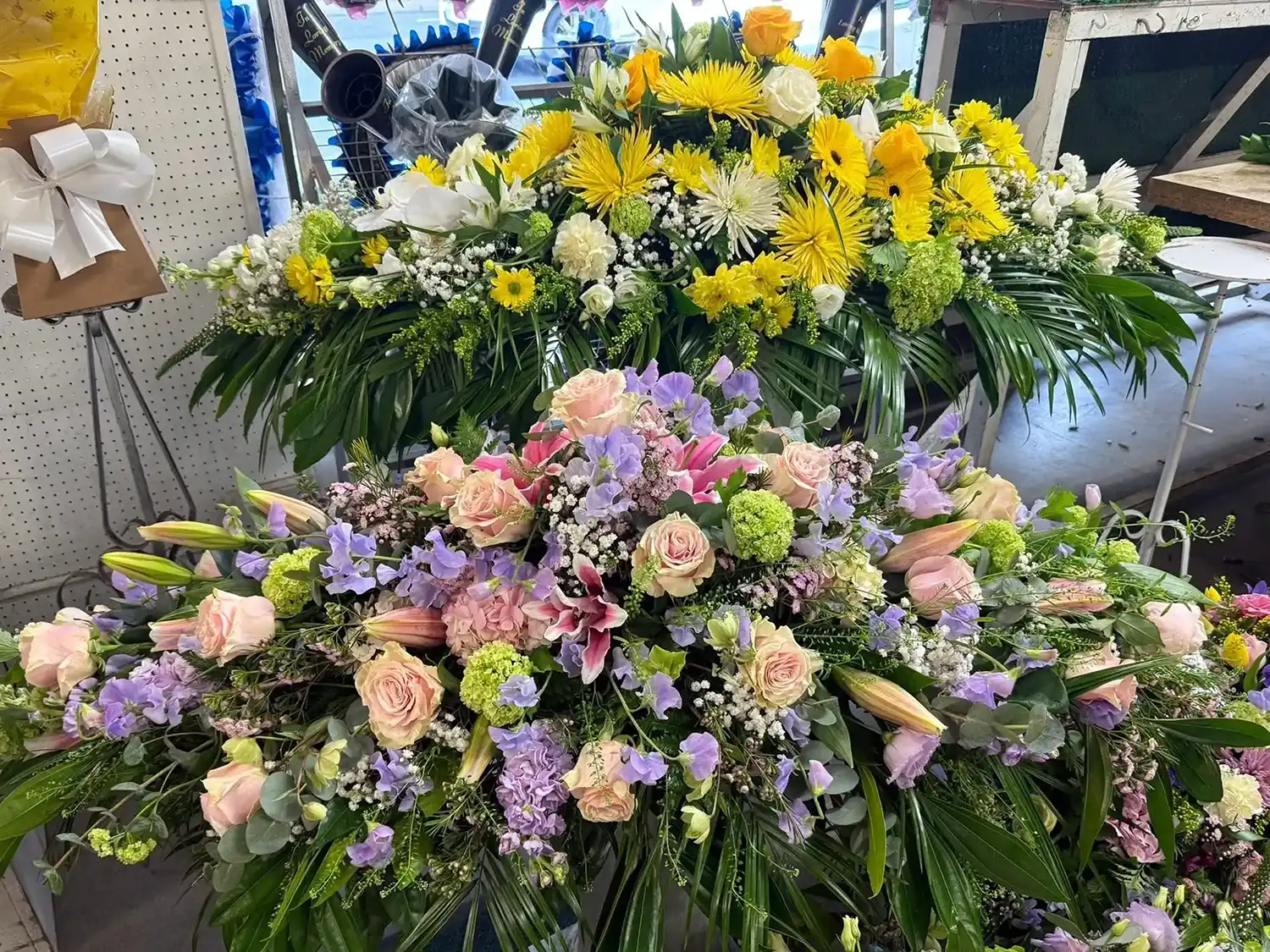 Two large funeral flower arrangements with yellow, white, pink, and purple blooms with green leaves.